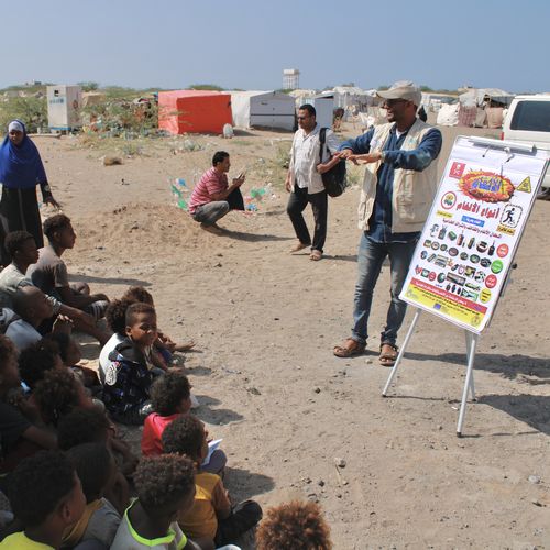 Ein HI-Mitarbeiter erklärt einer Gruppe Menschen anhand von Infotafeln, wie sie sich vor Blindgängern schützen können.