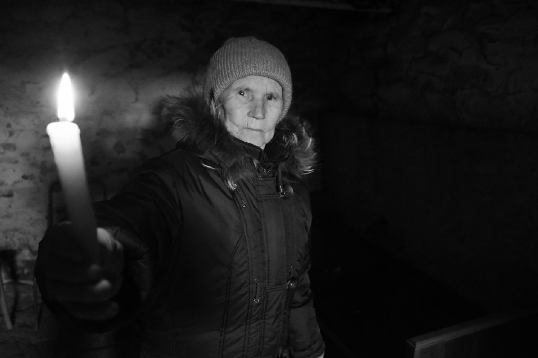 Eine ältere Frau leuchtet sich den Weg mit einer Fackel, sie schaut dabei ernst in die Kamera.