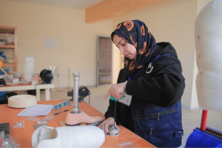 Ein kleiner Junge auf Krücken steht zwischen drei Mitarbeitenden von HI in einem Flüchtlingslager in Gaza.