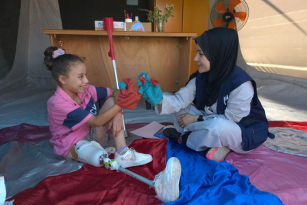 Ein kleines Mädchen, deren rechtes Bein unterhalb des Knies amputiert werden musste, sitzt zusammen mit ihrer Mutter auf dem Boden.