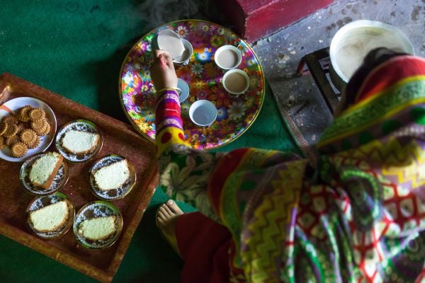 A teenage girl with a prosthetic leg sits on the floor with tea and cakes on trays