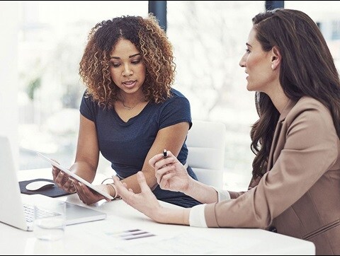 Two female colleagues discussing work over a laptop and a tablet