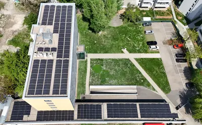 Luftaufnahme eines Gebäudedachs mit Solarpaneelen, angrenzend an eine grüne Wiese und einen Parkplatz.