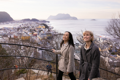Two students walking up a stair outside with the city of Ålesund in the background