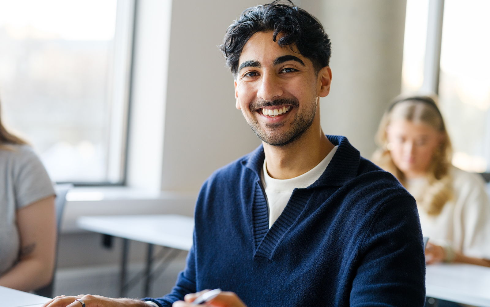 Glad mannlig student i forelesningsrom, med studenter bak ham