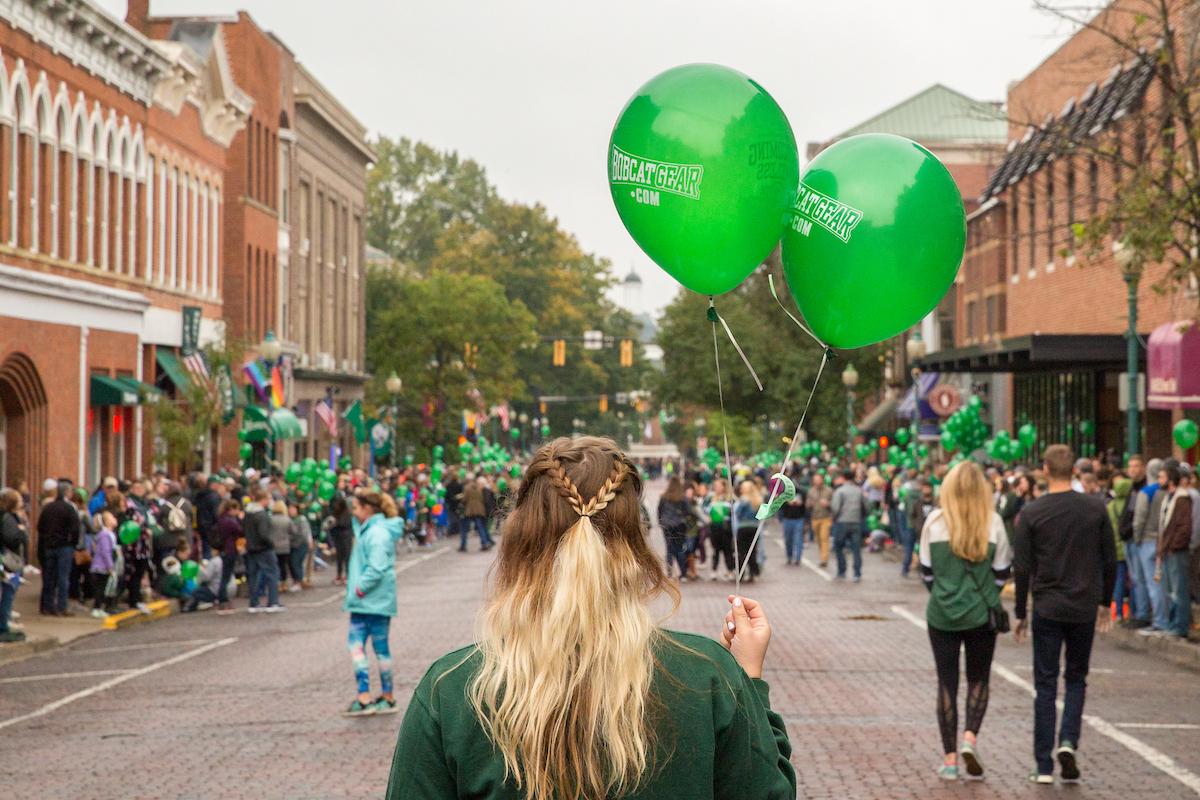 Person holds two green balloons on Court Street in Athens, Ohio