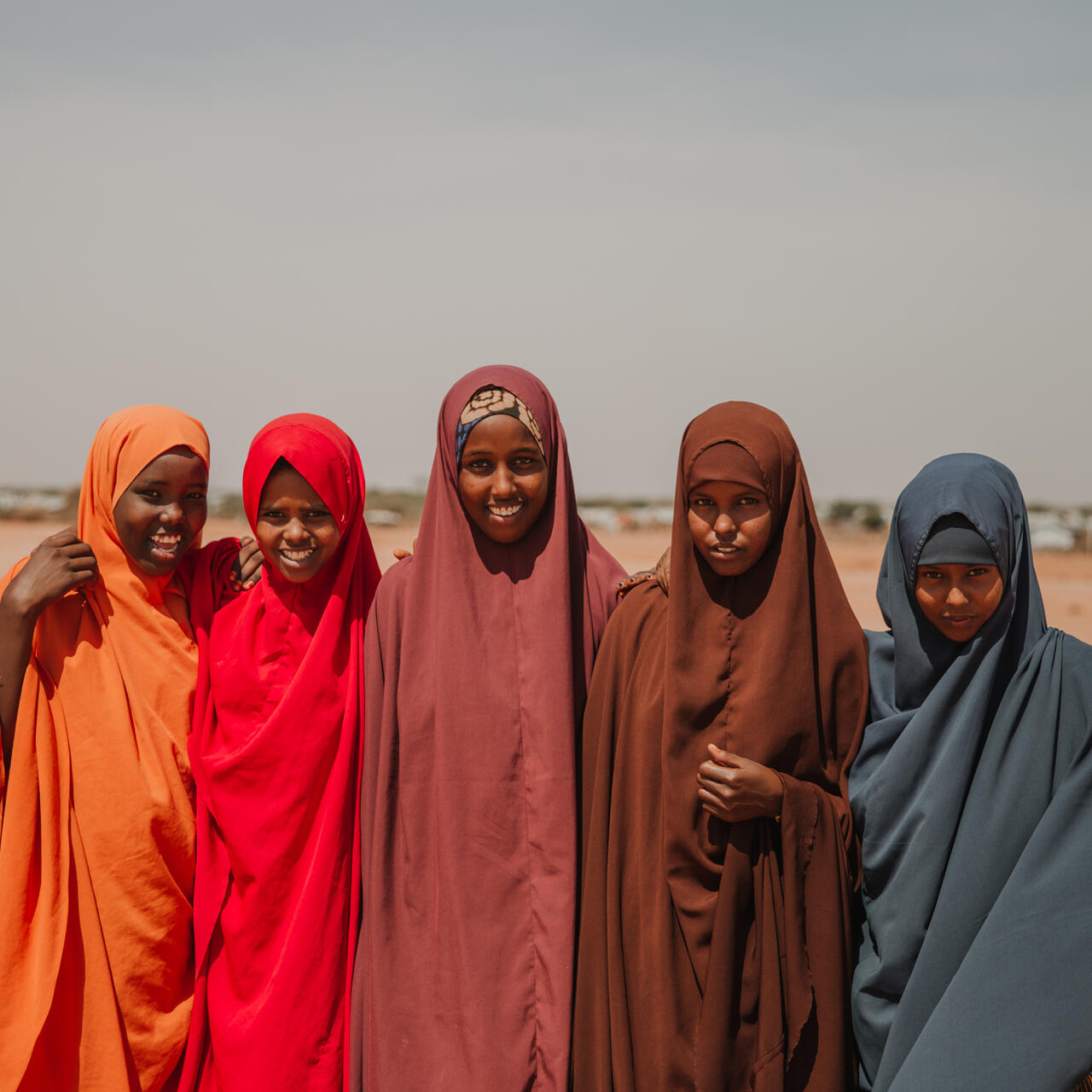 Five girls dressed in bright colours smile at the camera.