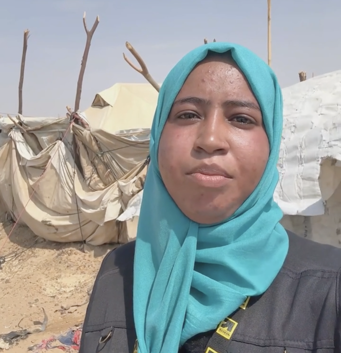 A woman wearing a blue hijab looks into the camera