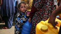 A young girl in Gaza stands by her parent as they collect safe water.