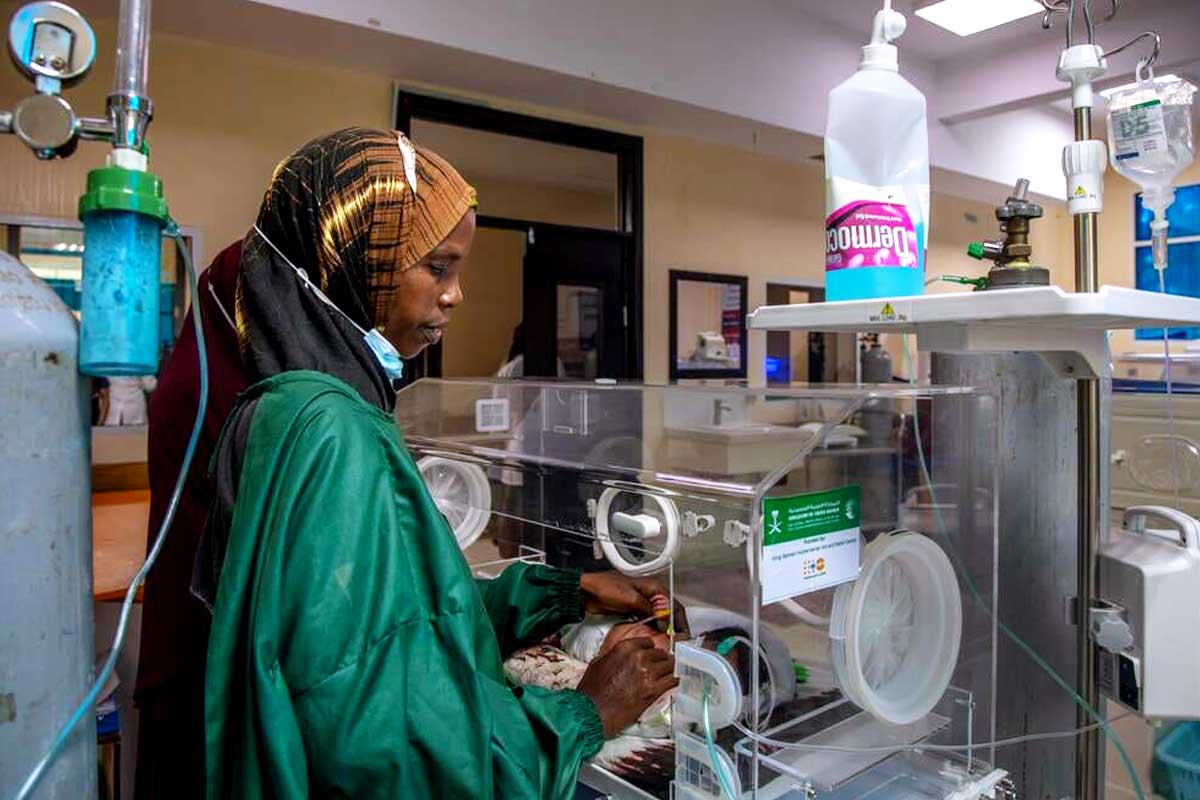 mother holds hand of a tiny baby through an incubator