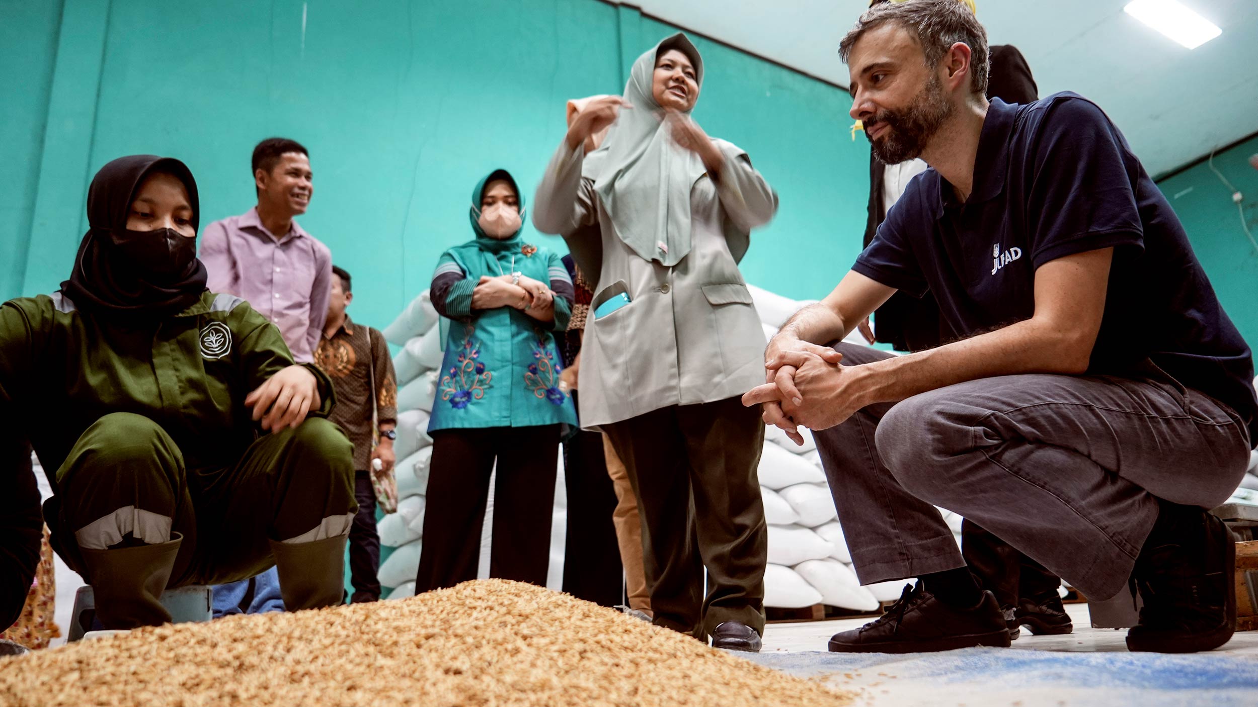 Alvaro kneels next to a mound of seeds and several women waeing viels plus a man are next to him