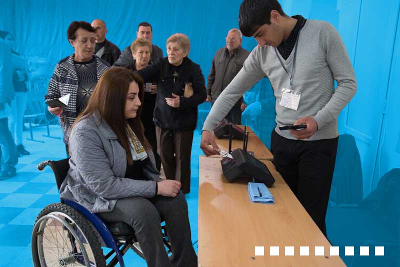 woman in wheelchair casts a vote while others, including senior citizens, wait their turn