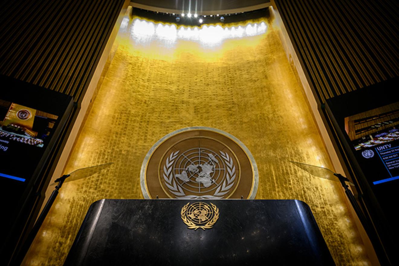 Podium of the General Assembly Hall seen from below with the gold wall and the golden UN logo behind