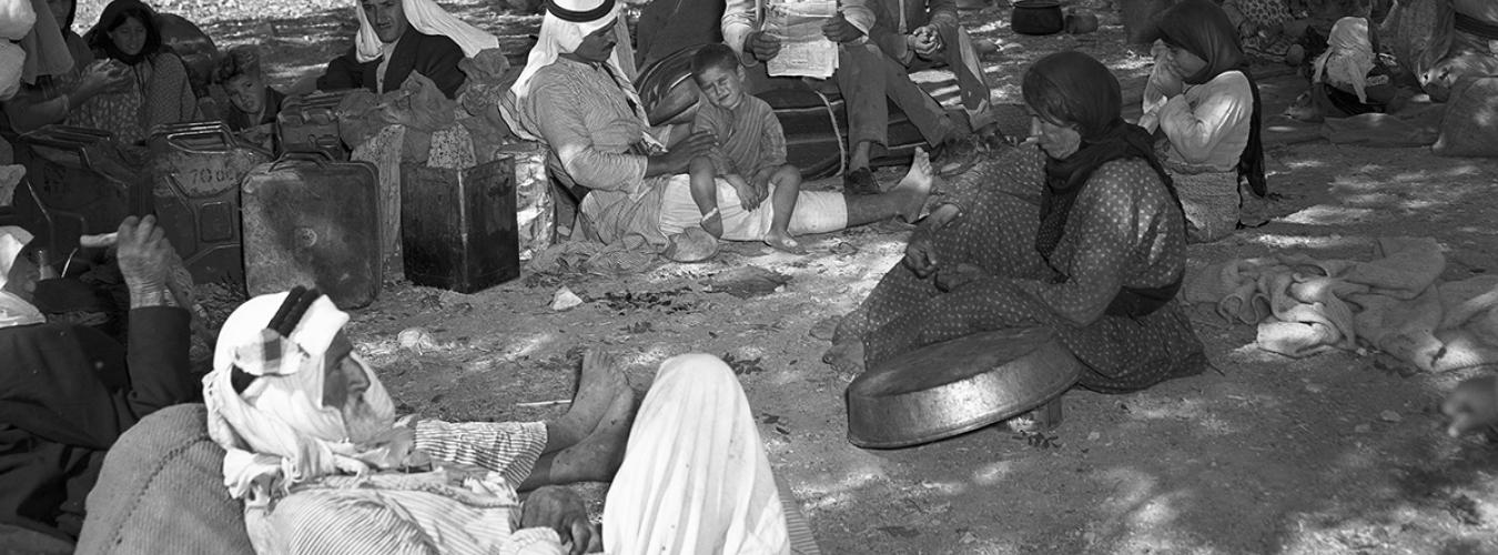 black and white photo of Palestinian refugees waiting seated on the ground