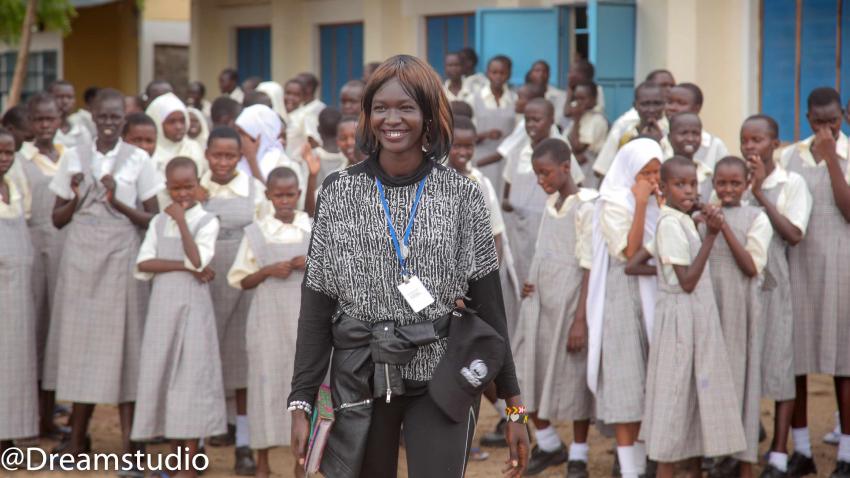 Mary poses for a photo with many young schoolkids in uniform seen standing behind her
