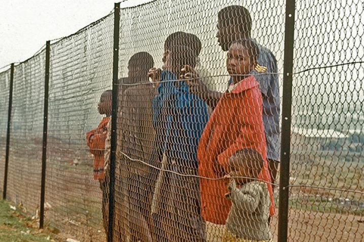 A group of South Africans behind fence separating them from white community.