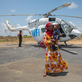 Eugenia Saide Luis, an employee of the Ibo Island Foundation, and her one-year-old son standing in front of an UNHAS helicopter in the city of Pemba, Cabo Delgado province