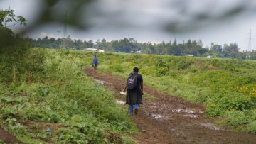A woman with backpack walking through a grassy field
