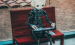 Ilustração de um robô de brinquedo preto e branco posicionado sobre uma mesa de madeira vermelha, em ambiente interno, com foco no objeto e fundo desfocado. | SciELO em Perspectiva Humanoid robot with a white head sitting on a wooden bench, reading a magazine inside a building with large windows nearby.