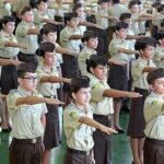 Contradições na opinião pública sobre a militarização das escolas estaduais em Goiás Fotografia de crianças com uniformes de escola militar e com um dos braços esticados para frente
