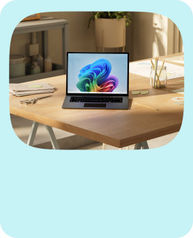 An open Windows laptop with the rainbow bloom screen sitting on a desk with office supplies surrounding it and furniture and a plant in the background