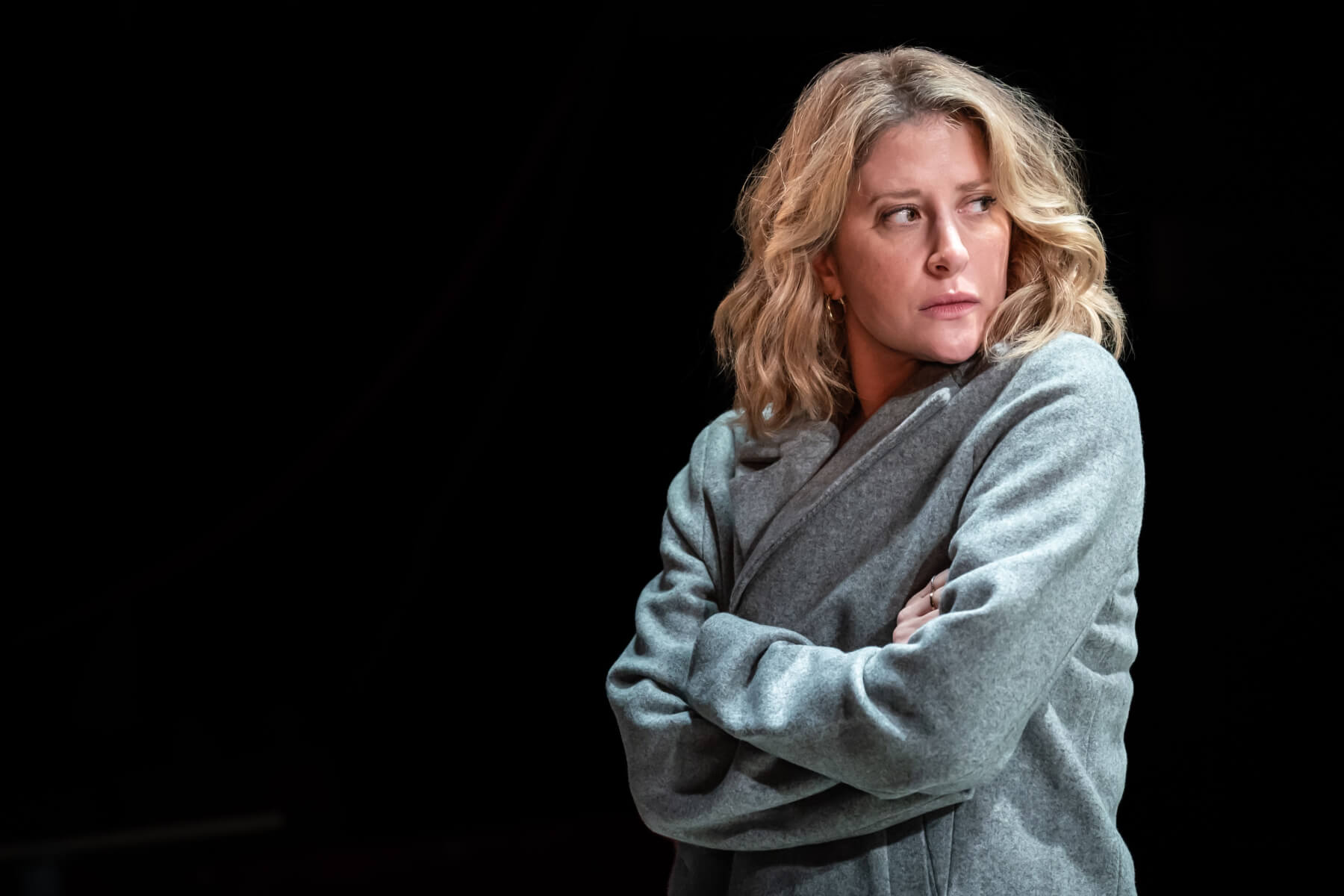 Diana, played by Caissie Levy, wearing a long-sleeved gray jacket staring to our right with a black background.