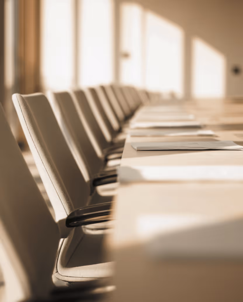 Row of beige office chairs along a conference table with sunlight streaming through windows.