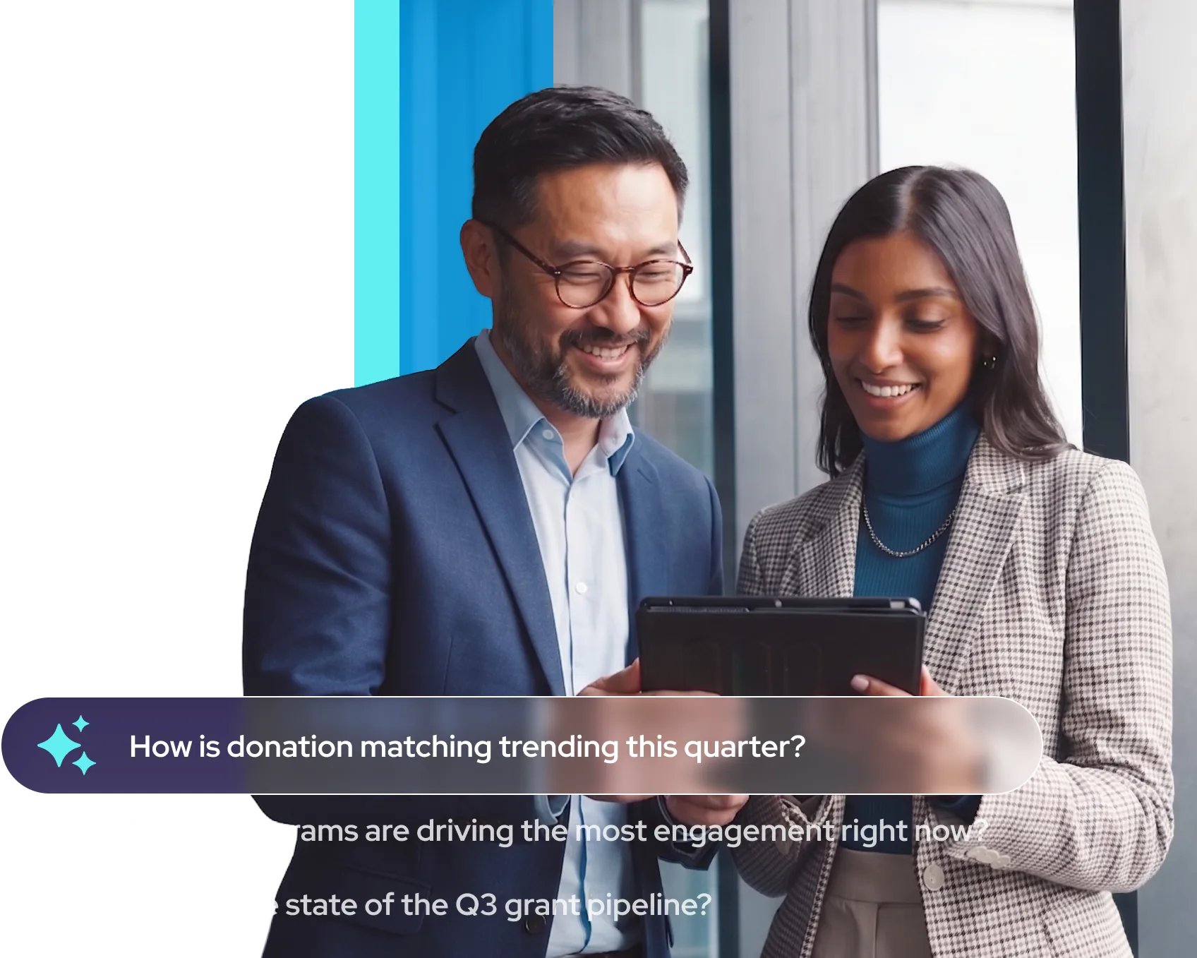 Smiling man and woman in business attire looking at a tablet in an office setting.