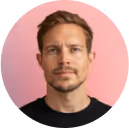 Portrait of a man with short light brown hair and a light beard against a pink background.