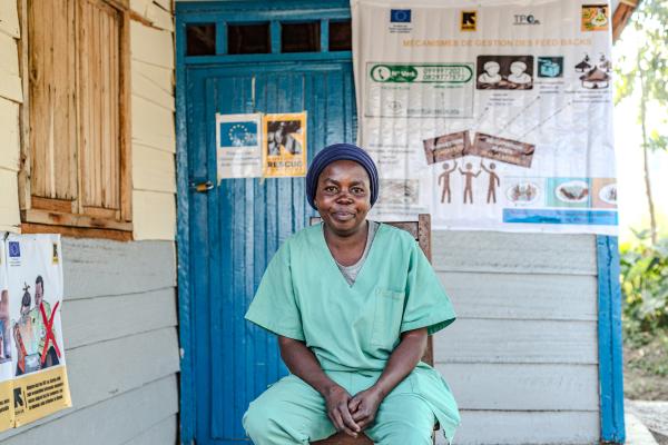 Medical practitioner dressed in green uniform sitting down outside a make-shift clinic