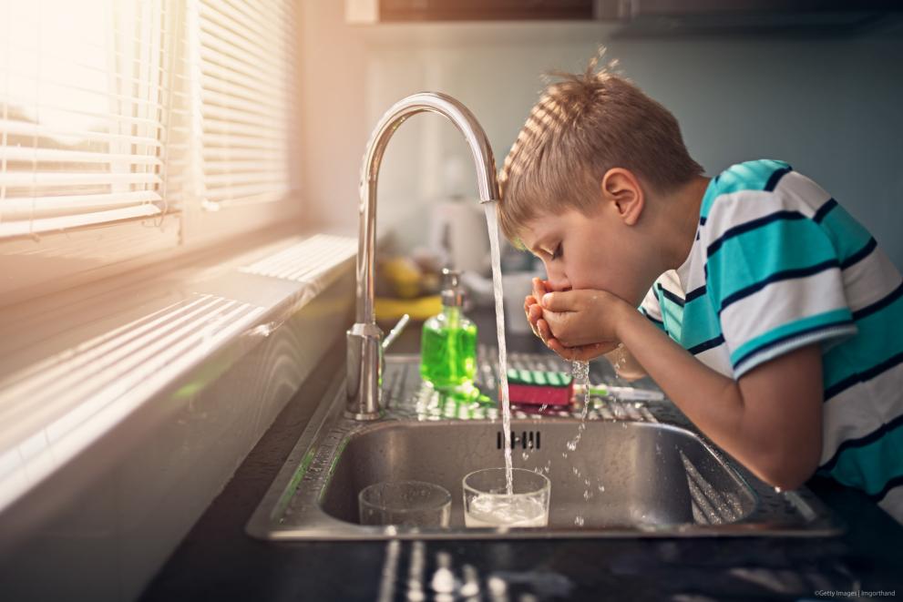 Little boy drinking tap water in the kitchen