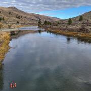 Small boat floats in river with dry grassy hills in background