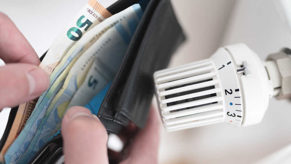 A person holding an open wallet beside a thermostat.
