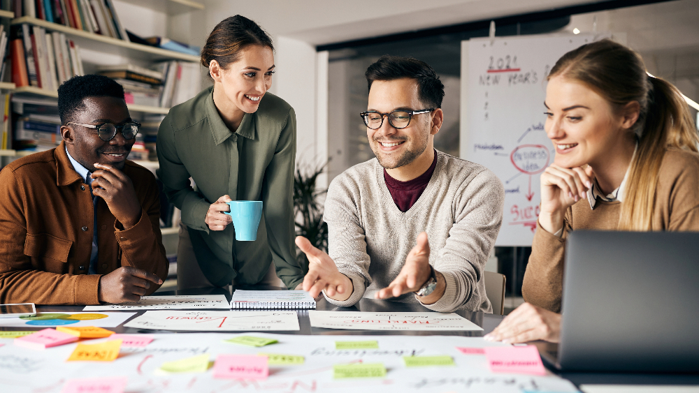 A group of people smiling while standing over the table with papers and post-its.