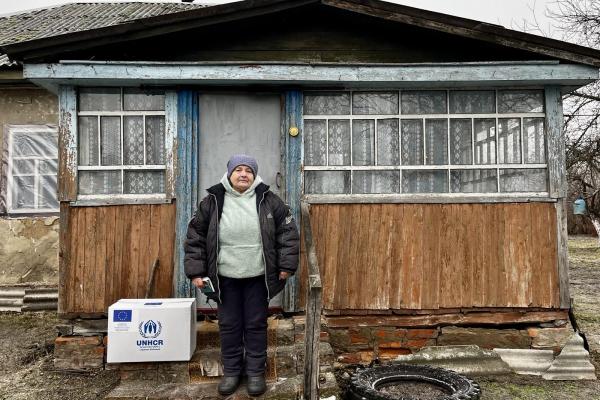Woman in jumper, jacket and wollen hat standing on steps of her house, Ukraine