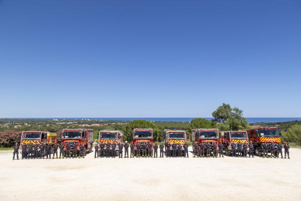 Romanian and French firefighters posing for a group photo in front of their fire trucks