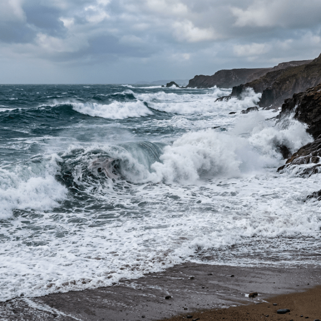 Strong ocean waves breaking on rocky coastline under cloudy sky