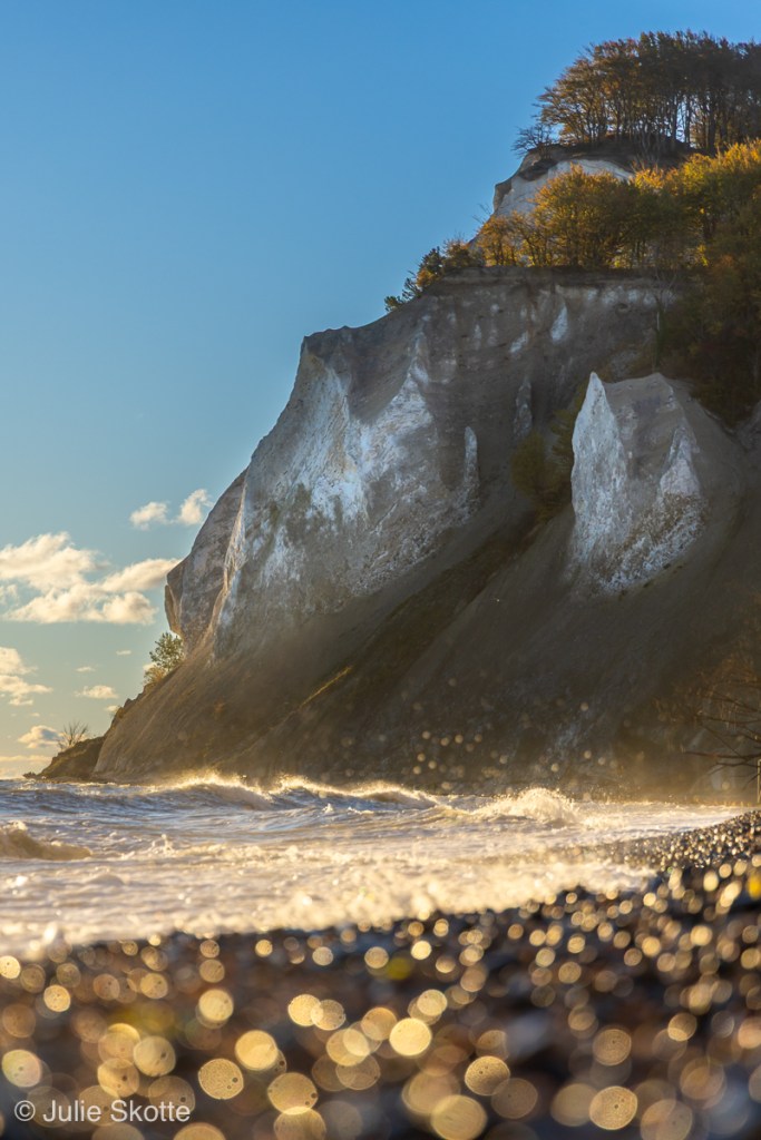 Møns Klint landskab En strand med bokeh bobler i forgrunden, en bølger der kommer i mod stranden og klinten i baggrunden.