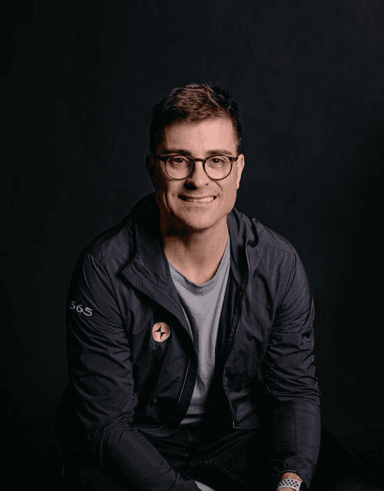 Person wearing glasses and a black jacket sitting indoors.