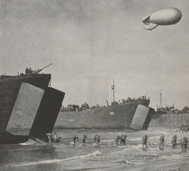 Des soldats américains descendent des rampes des péniches de débarquement dont l'avant s'est ouvert pour les laisser passer. Ils progressent avec de l'eau jusqu'aux genoux.