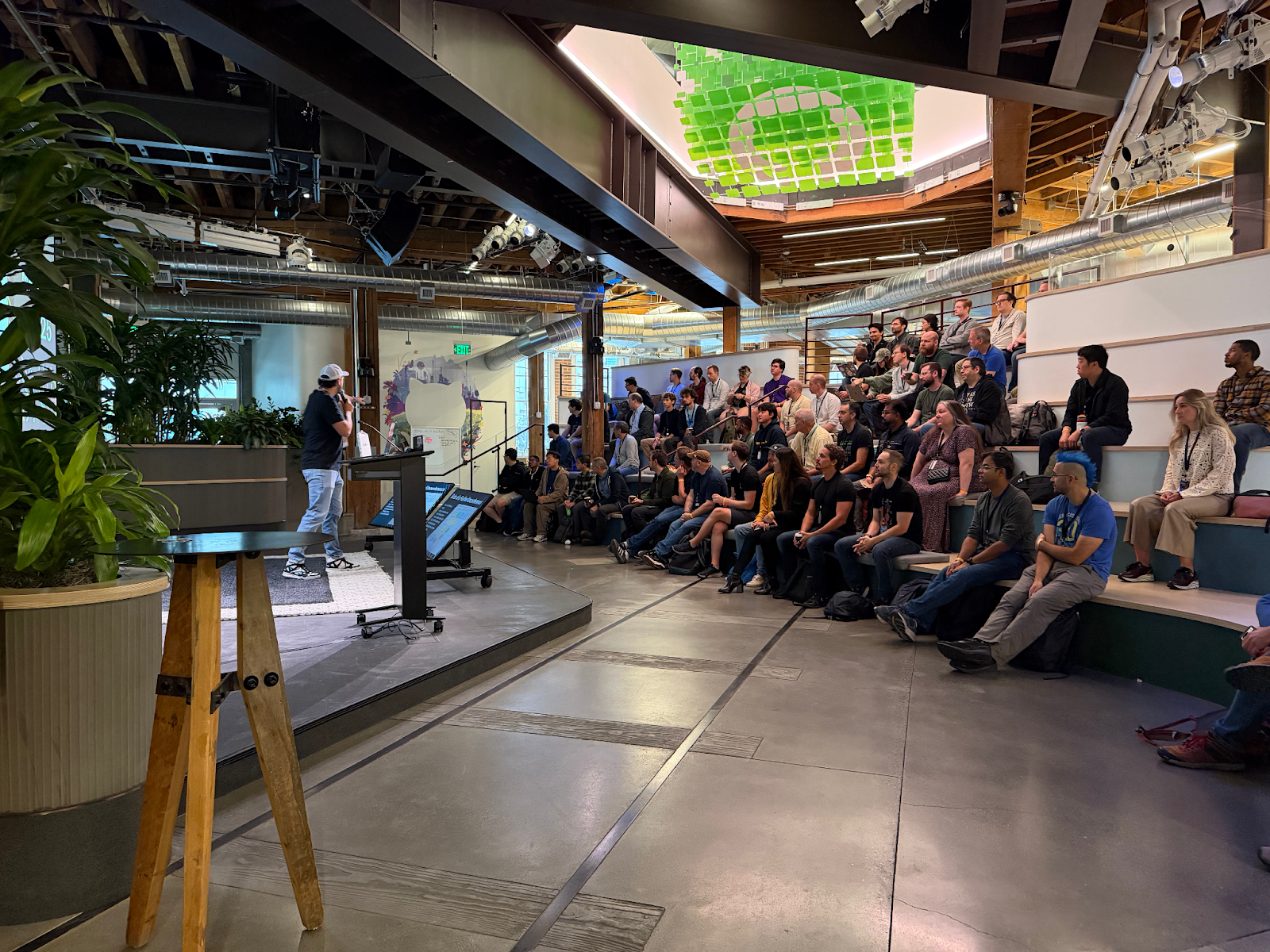 People seated around a long conference table at GitHub HQ’s Executive Briefing Center during the Git Contributors Summit. Laptops are open, and several participants join remotely on large screens at the front of the room.