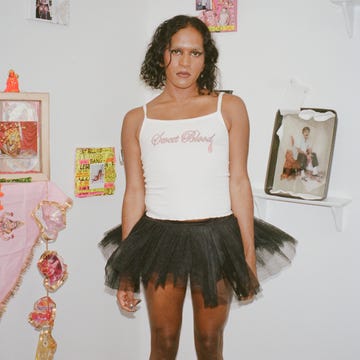 Person in a black tutu and white tank top standing against a decorated wall. Person in a black tutu and white tank top standing against a decorated wall.