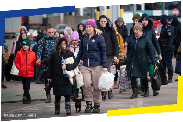 The photograph shows displaced people crossing the border from Ukraine into the EU. We see mainly women with children carrying small bags with their belongings. The image is framed into two brackets in the blue and yellow colors of the Ukrainian flag. At the bottom left there is a hashtag: EU stands with Ukraine. 