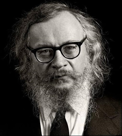 Black and white photograph of Jerzy Grotowski, a white man with medium-length white hair, beard and moustache, wearing glasses and a black suit and tie. Black and white photograph of Jerzy Grotowski, a white man with medium-length white hair, beard and moustache, wearing glasses and a black suit and tie.