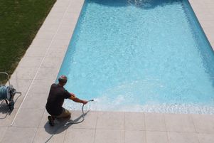 Un homme remplit une piscine privée avec un tuyau d’arrosage.