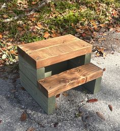 a wooden bench sitting on top of a cement ground next to grass and leaves in the background