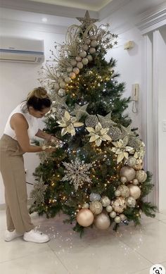 a woman decorating a christmas tree with gold and silver ornaments