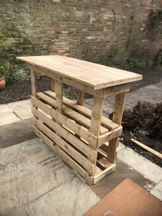 a table made out of wooden pallets sitting on top of a cement floor next to a brick wall