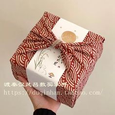 a hand holding a wrapped gift box with a red and white bow on it's side