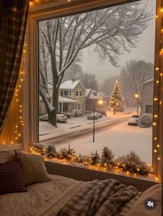 a bedroom window with christmas lights on the windowsill and a view of a snowy street